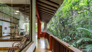 A corridor with a wooden bench, glass walls, and a view of dense greenery outside. - Casa Iporanga (Guarujá)