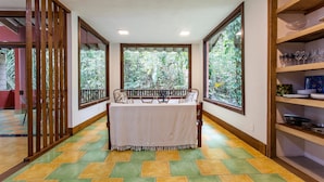A dining area with a table set for two, large windows with a view of greenery, and a tiled floor with a geometric pattern. - Casa Iporanga (Guarujá)
