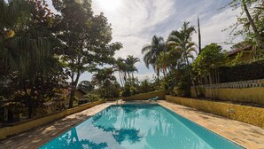 A rectangular swimming pool with tiled edges, surrounded by a paved walkway and lush tropical vegetation. - Chácara Master - O Melhor de Guararema (Guararema)