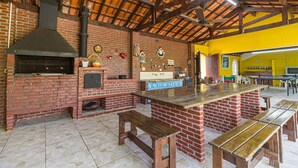 A rustic kitchen with a brick fireplace, wooden benches, and a yellow wall. - Chácara Master - O Melhor de Guararema (Guararema)