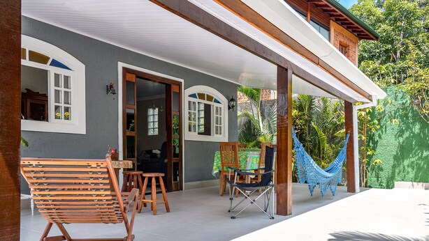 A covered patio with wooden furniture, a hammock, and a dining area with a table and chairs. - Casa Viela da Paz (Ilhabela)