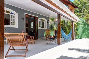 A covered patio with wooden furniture, a hammock, and a dining area with a table and chairs. - Casa Viela da Paz (Ilhabela)