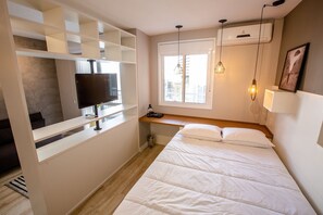A bedroom with a bed, a TV, a window, and a built-in shelf.