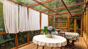 A wooden deck with a round table and chairs, a white tablecloth, and a potted plant with purple flowers. -  Vale do Lajeado - Campos do Jordão (Campos do Jordão)