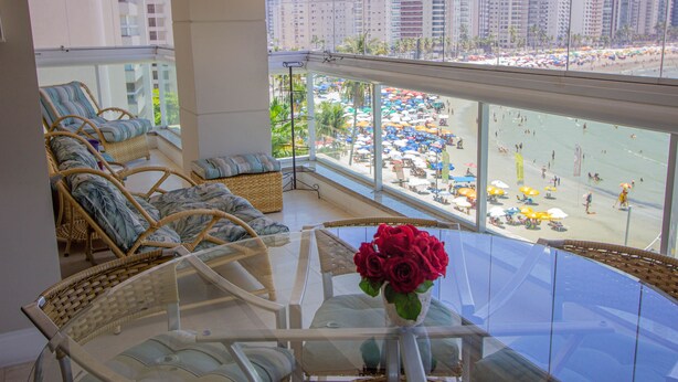 Varanda com móveis de vime e uma mesa de vidro com um vaso de rosas vermelhas.