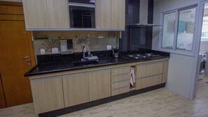 Cozinha com armários de madeira, bancada preta e janela com persianas.