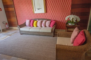 Uma sala de estar com sofá e poltrona, parede estampada, quadro emoldurado e mesa de centro com um vaso de flores.