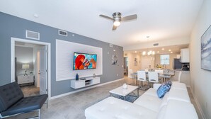 A modern living room with a white sofa, a black armchair, and a flat-screen TV mounted on the wall. - (FR304) Storey Lake Condo 2/2, Free Waterpark (Kissimmee)