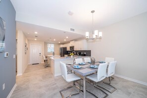 Una cocina moderna con armarios blancos, una isla central y un comedor con mesa y sillas.