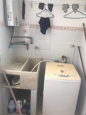 Ein kleiner Waschbereich mit einer Waschmaschine, einem Waschbecken und einem Wäscheständer.