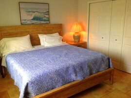 Una cama con una colcha azul con textura, un cabecero de madera, almohadas blancas y una mesita de noche con una lámpara.
