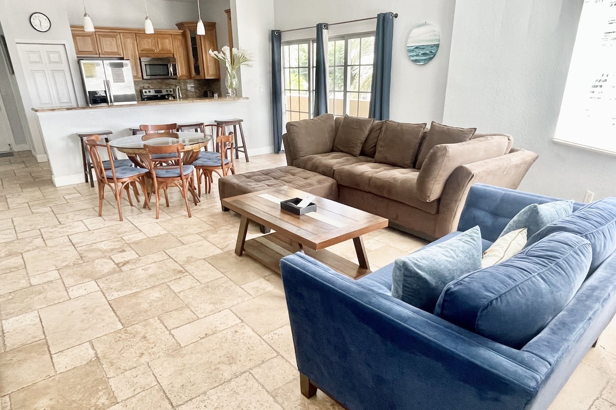 A spacious living area with a blue sofa, a brown sofa, a wooden coffee table, and a dining table with chairs.