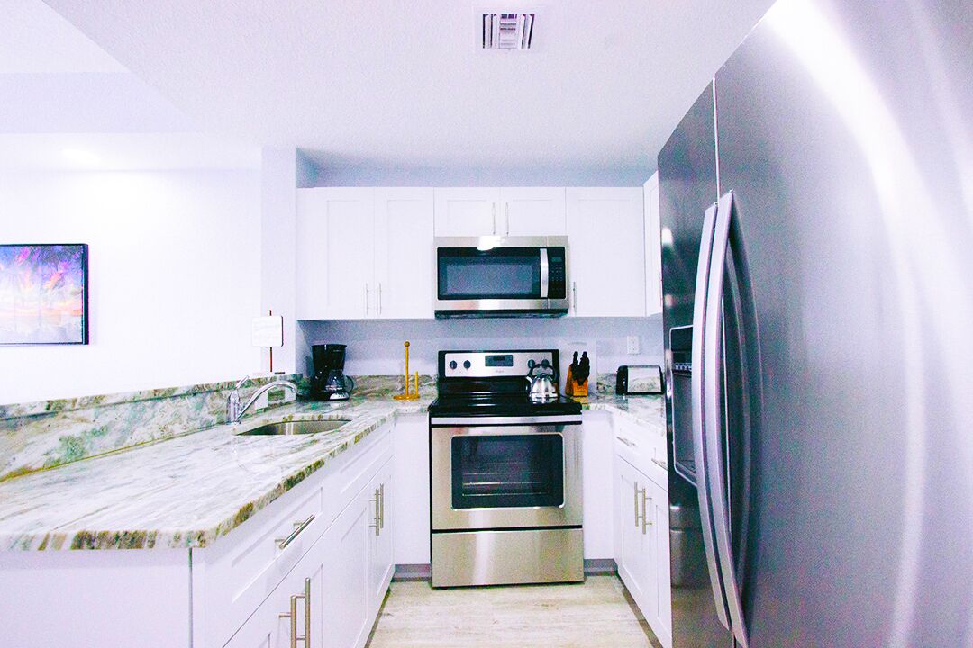 A modern kitchen with white cabinets, stainless steel appliances, a marble countertop, and a large refrigerator.