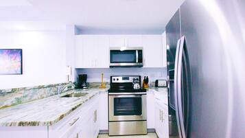 A modern kitchen with white cabinets, stainless steel appliances, a marble countertop, and a large refrigerator.