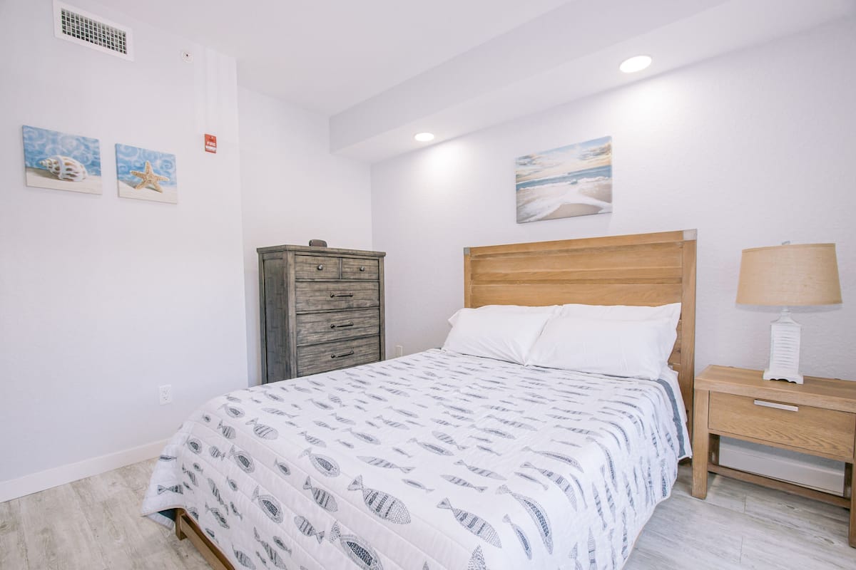 A bedroom with a bed, a wooden nightstand, a dresser, and wall art.