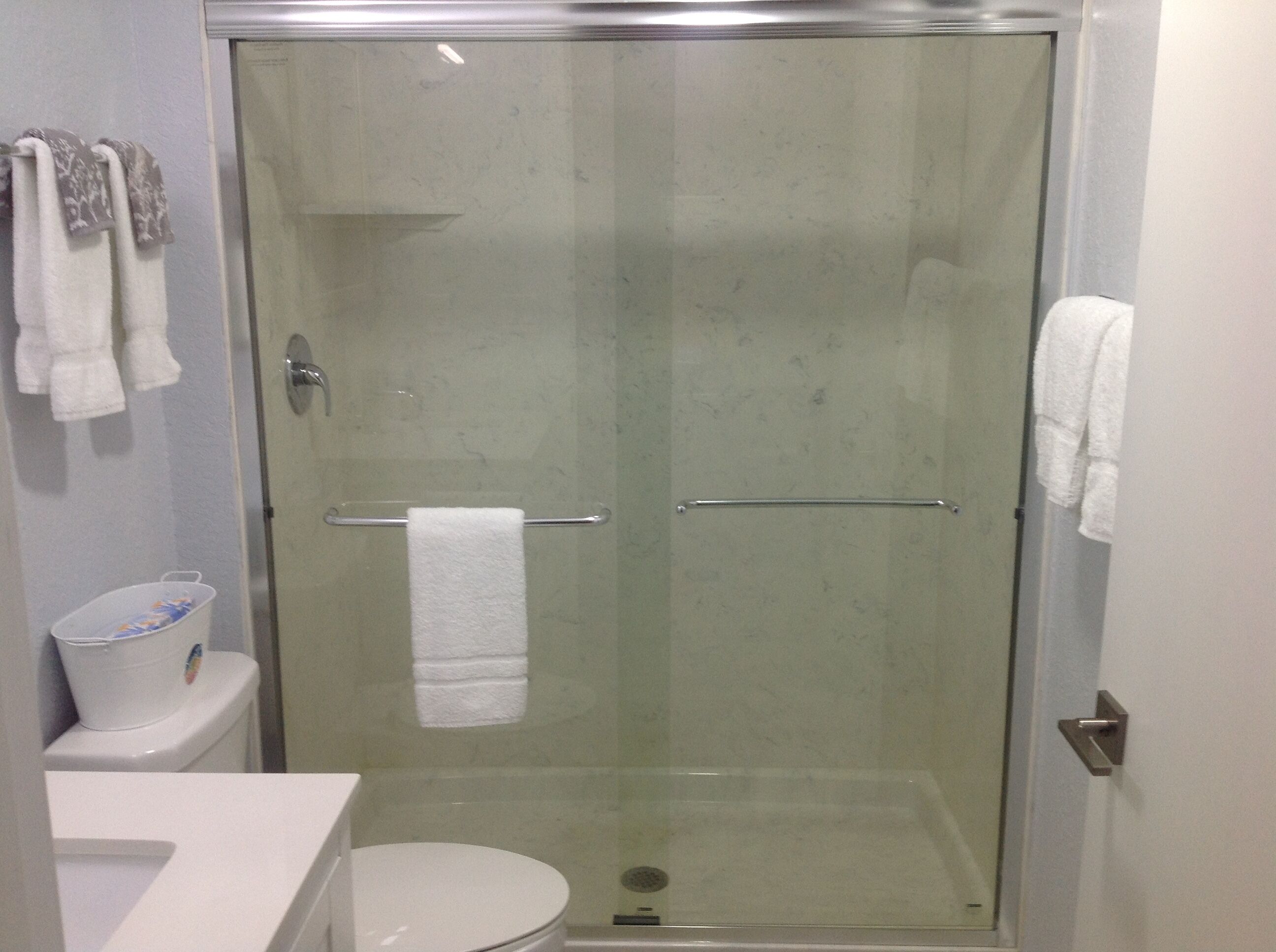 Une cabine de douche fermée par des parois de verre, avec une serviette blanche suspendue à une barre métallique.