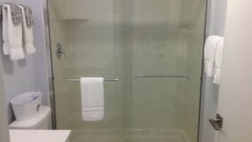 A glass-enclosed shower stall with a white towel hanging on a metal bar.