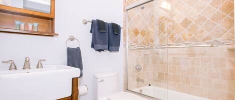 Een badkamer met een wit wastafelmeubel, een toilet en een douche met glazen wanden.