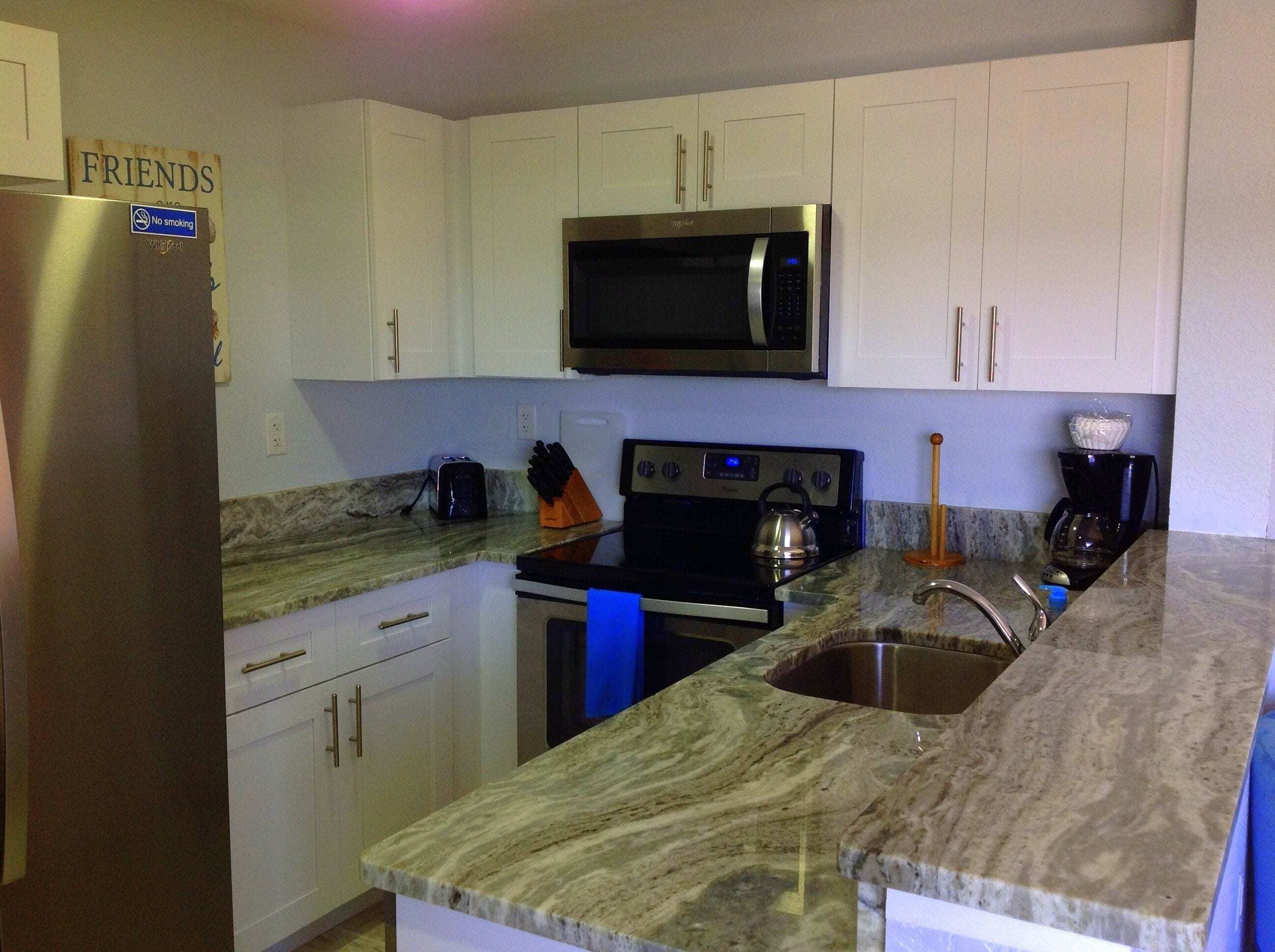 A kitchen with white cabinets, a stainless steel refrigerator, a microwave, a stove, and a sink.