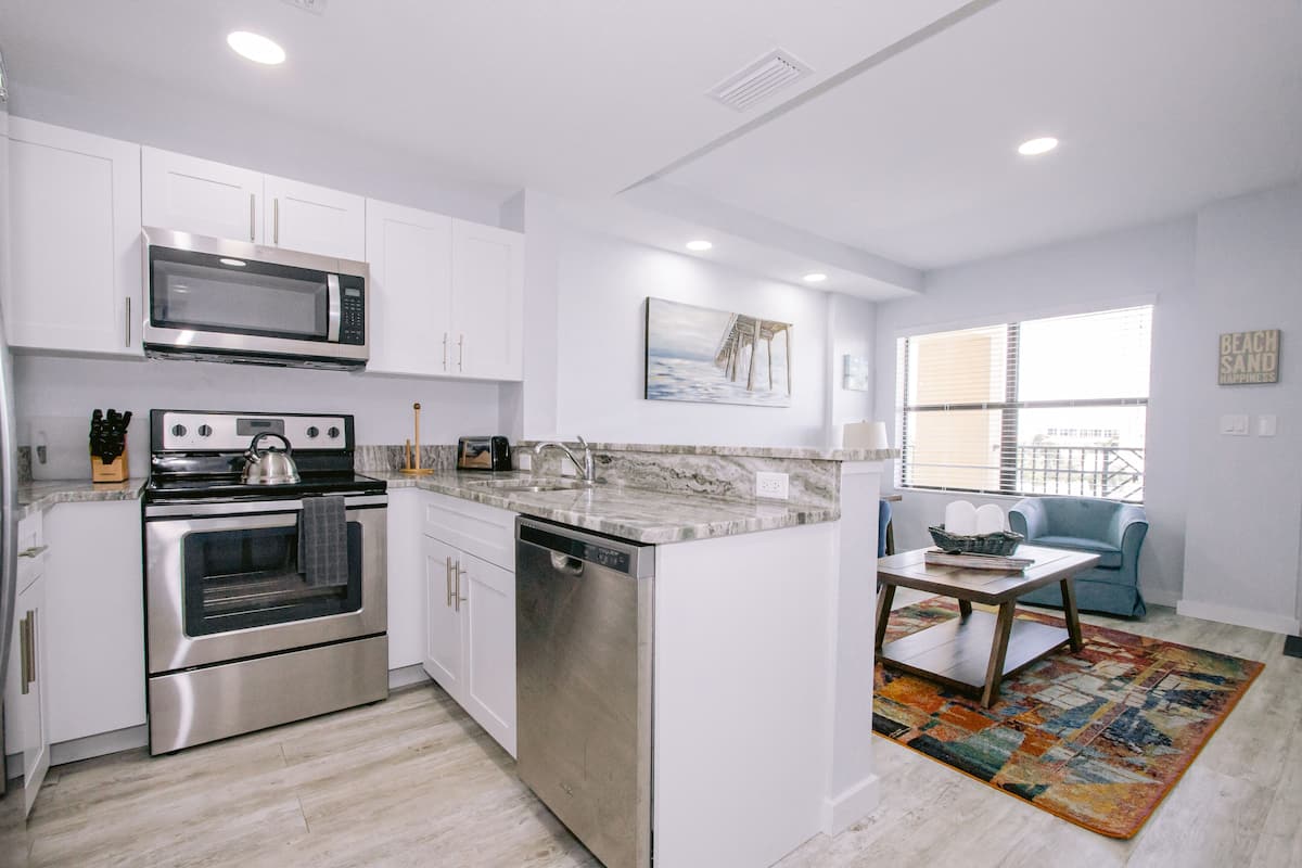 A modern kitchen with white cabinetry, stainless steel appliances, and a marble countertop.