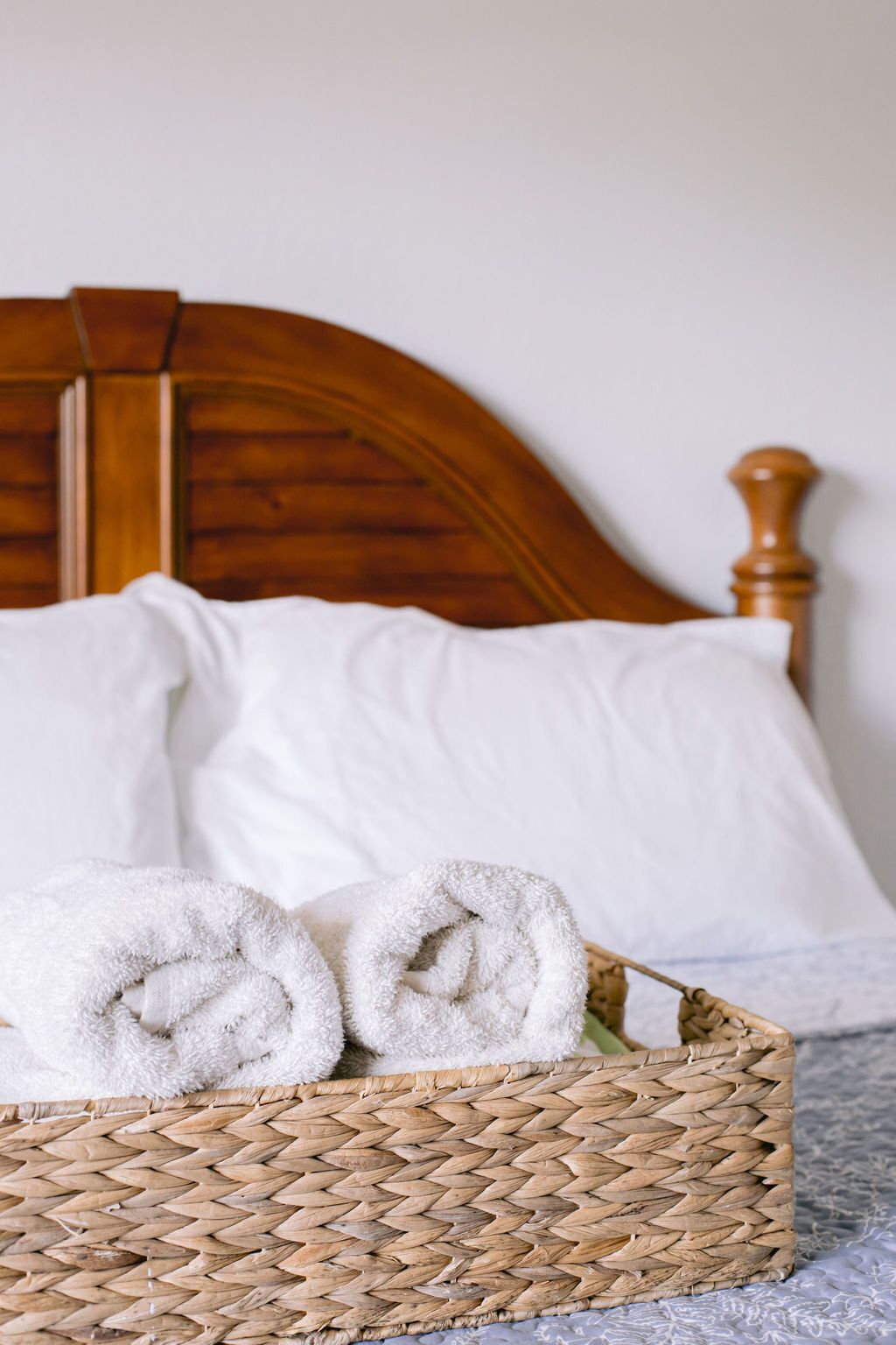 A bed with a wooden headboard, white linens, and a woven basket with folded towels.