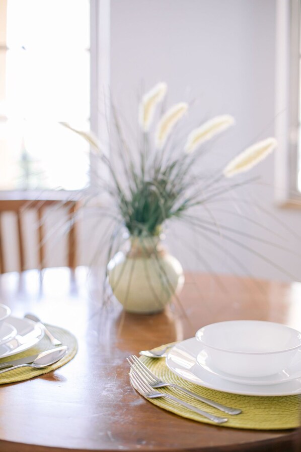 A dining table with a white vase of white flowers, a wooden chair, and a window in the background.
