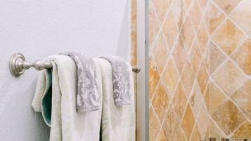 A bathroom with a glass shower door, a towel rack with two towels, and a tiled wall.