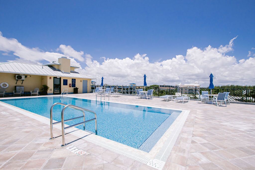 A swimming pool with lounge chairs and umbrellas, a building with a metal roof, and a clear blue sky.