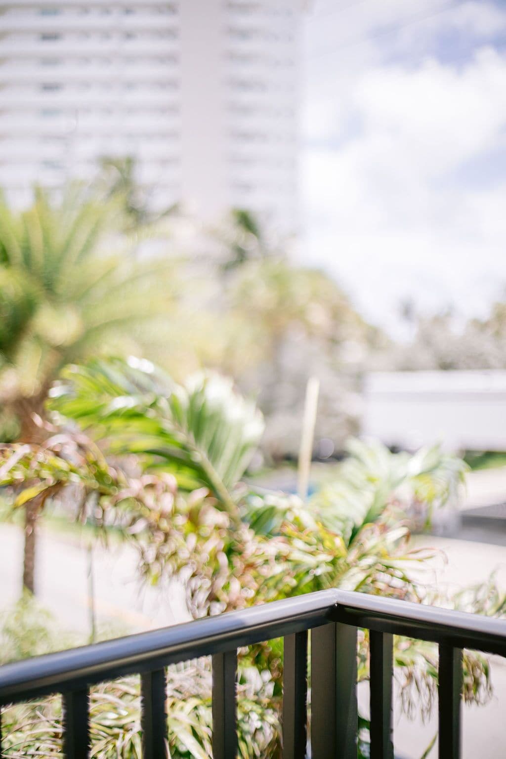 A balcony with a railing, overlooking a cityscape with buildings and palm trees.