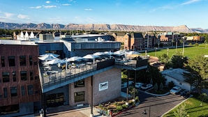 A modern building with a rooftop patio area, a sign for 'Devi's Kitchen', and a parking lot with cars. - Hotel Maverick (Grand Junction)