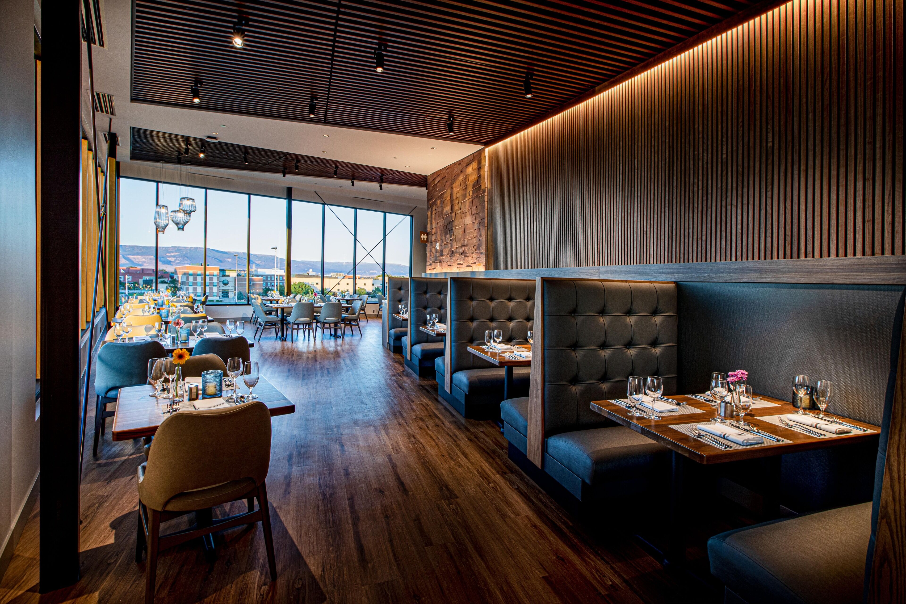 Ein modernes Restaurant mit Holzboden, hohen Decken und großen Fenstern mit Blick auf die Stadt.