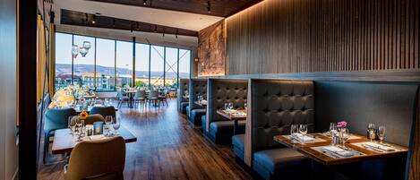 Ein modernes Restaurant mit Holzboden, hohen Decken und großen Fenstern mit Blick auf die Stadt.