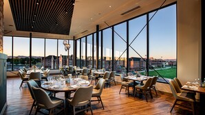 A modern restaurant with large windows offering a city view. Tables are set with dinnerware. - Hotel Maverick (Grand Junction)