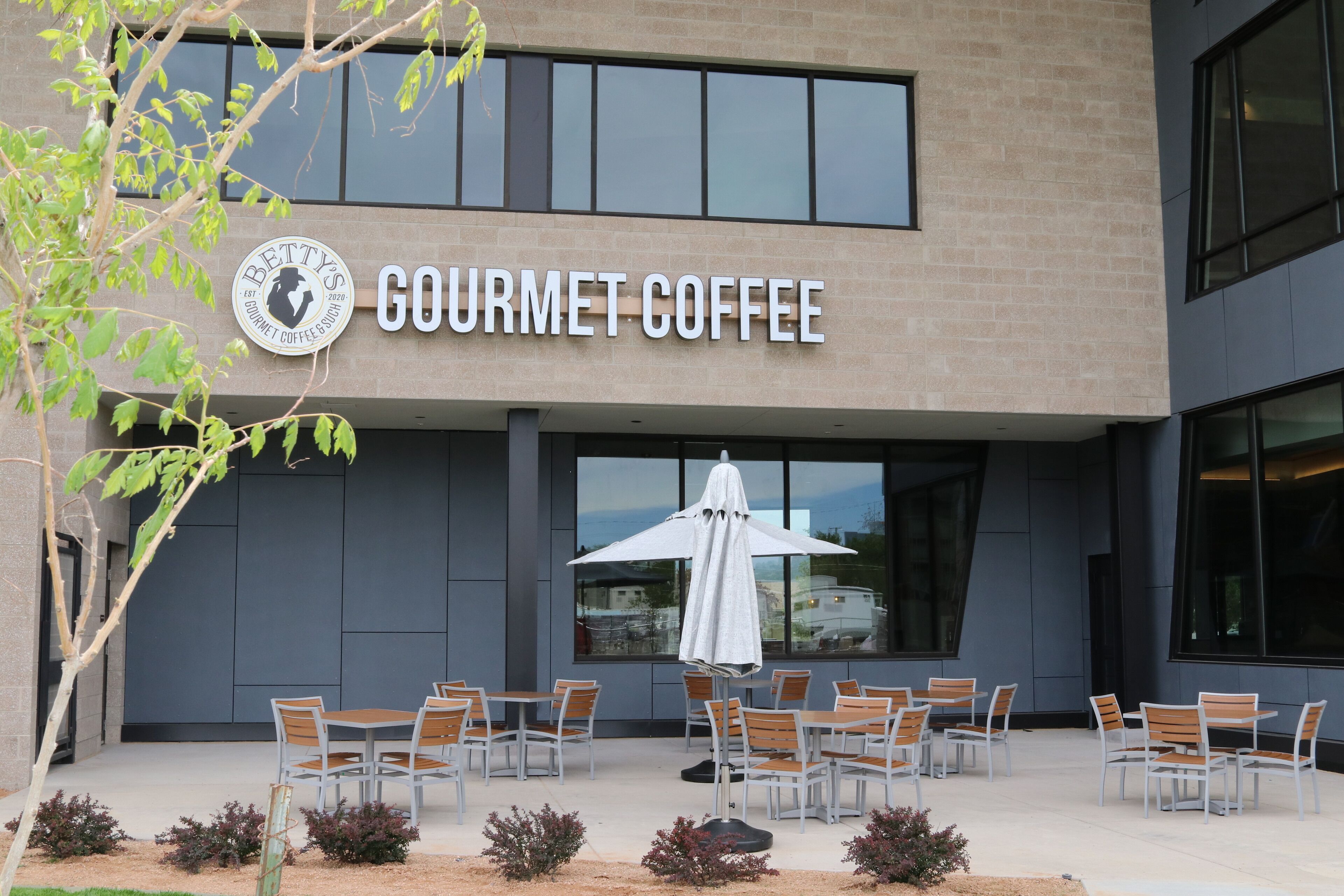 A building with a sign reading "Gourmet Coffee" and outdoor seating with umbrellas.