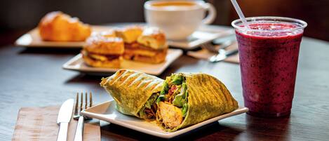 Un almuerzo con un wrap, una taza de café y un batido sobre una mesa de madera.