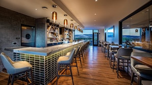 A modern bar area with a long counter, bar stools, and a view of the outdoors. - Hotel Maverick (Grand Junction)