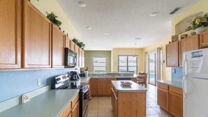 A spacious kitchen with wooden cabinets, a central island, and a refrigerator. - Fun Family Escape: 6 BR Oasis w/Private South-Facing Pool! (Davenport)