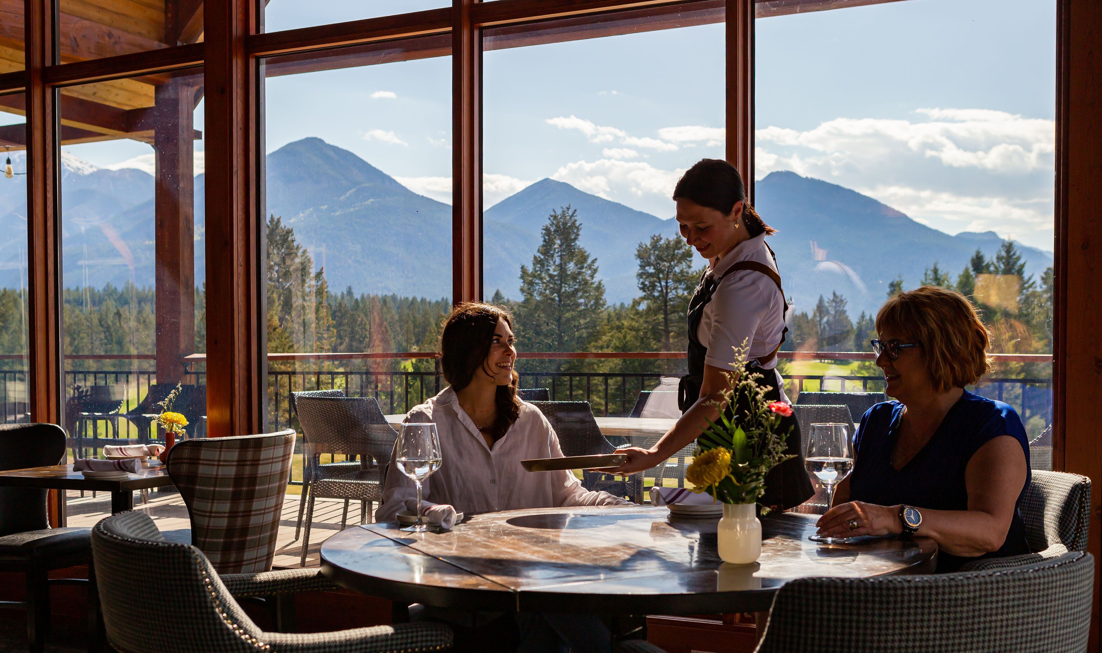 A restaurant with a mountain view, large windows, and outdoor seating.