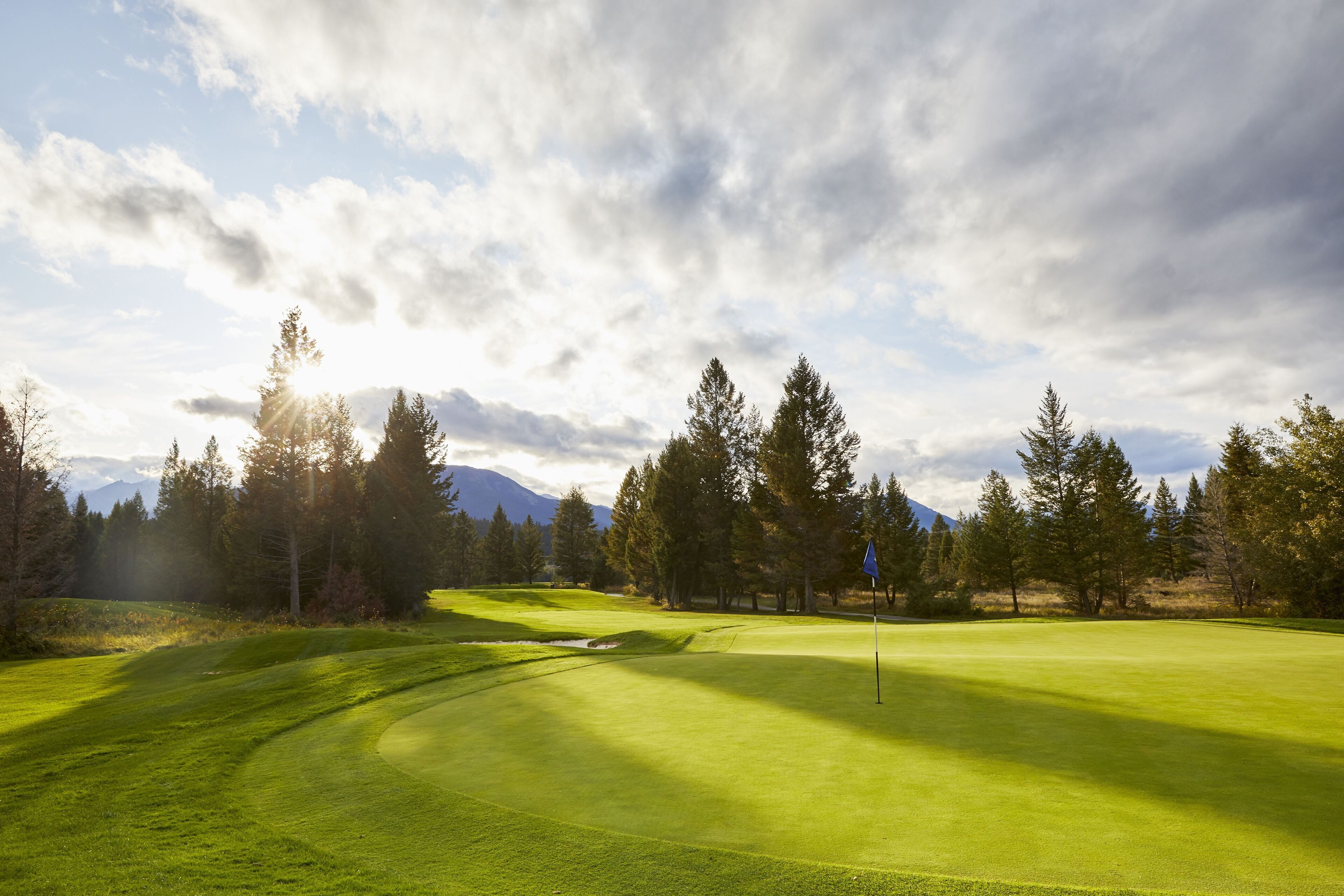 Un terrain de golf avec un drapeau, des arbres et des montagnes en arrière-plan.