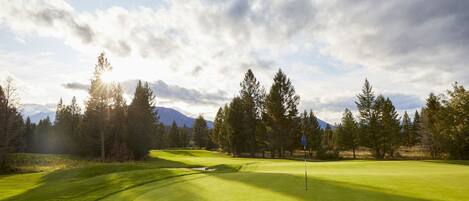 Un terrain de golf avec un drapeau, des arbres et des montagnes en arrière-plan.
