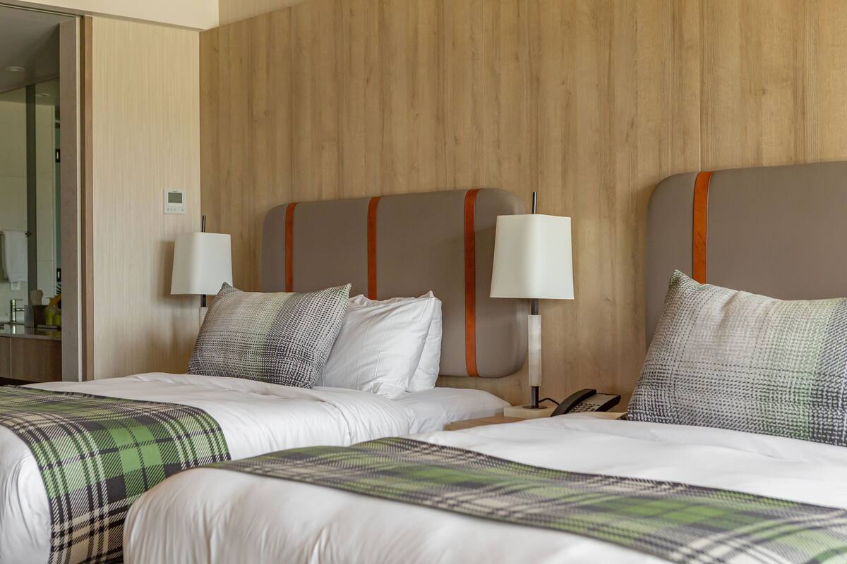 A hotel room with two beds, wooden headboards, white bedding, and bedside lamps.