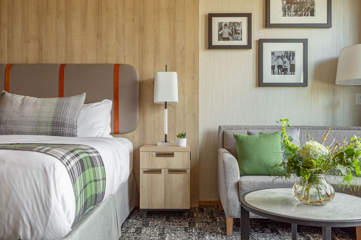 A hotel room with a bed, a nightstand with a lamp, a sofa, and a coffee table with a vase of flowers.