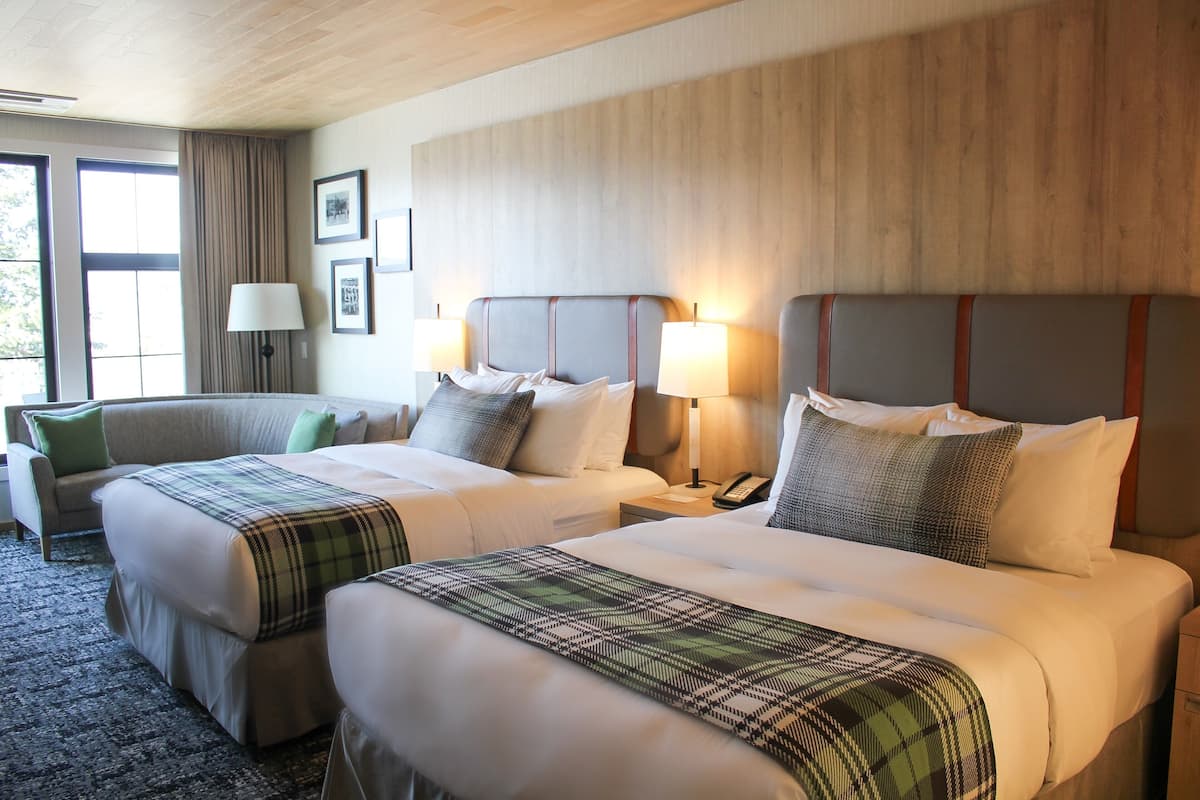 A hotel room with two beds, a sofa, a lamp, and a window with curtains.