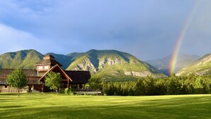 A lodge with a wooden exterior, a covered porch, and a view of mountains and a rainbow. - Headwaters Lodge at Eagle Ranch Resort (Invermere)
