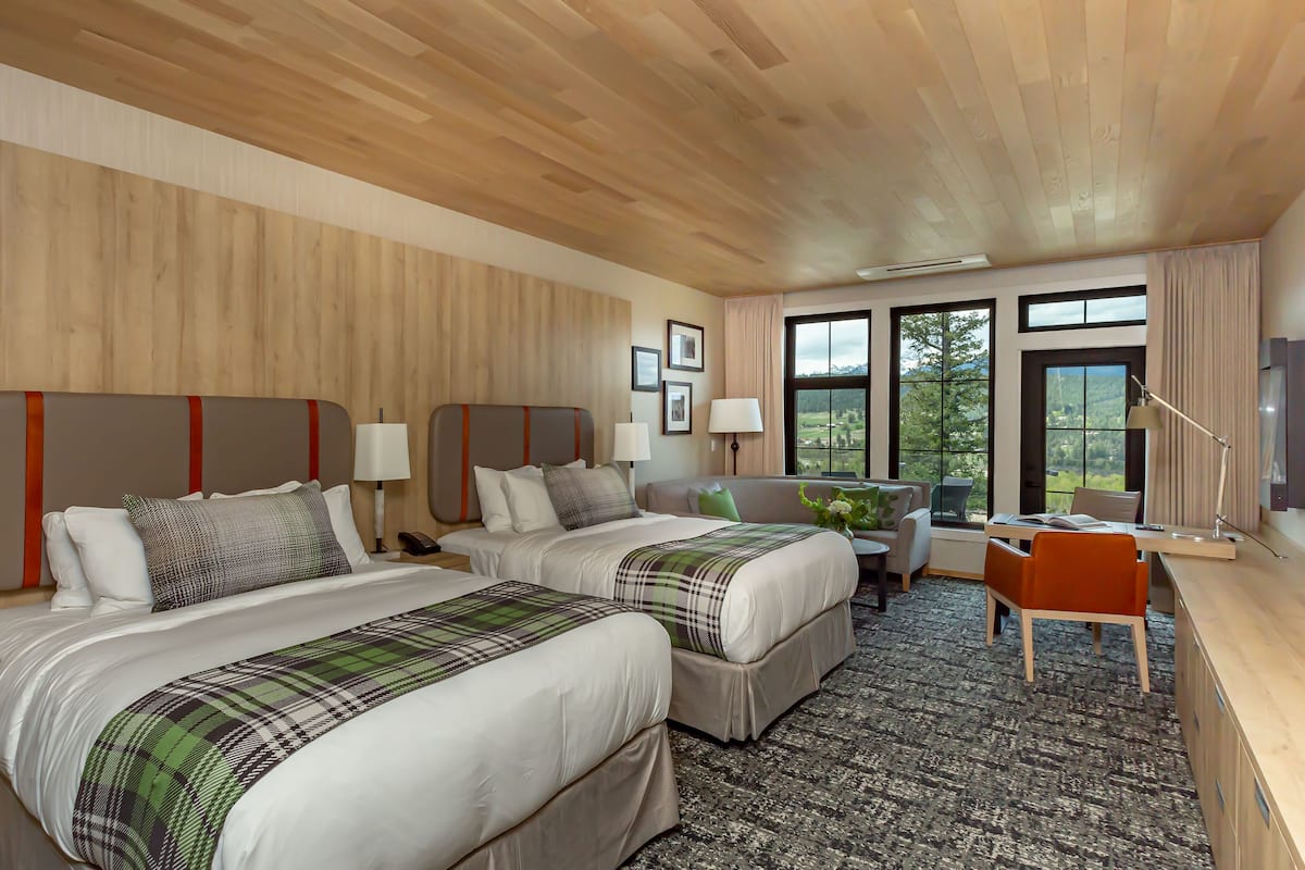 A hotel room with two beds, a desk, a chair, and a view of the outdoors.