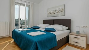 A bedroom with a bed, a nightstand, a window with curtains, and a painting on the wall.