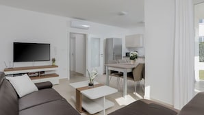 A modern living room with a large flat-screen TV, a sofa, a coffee table, and a dining area with a kitchen in the background.