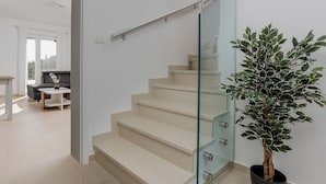 A modern staircase with glass railings and beige steps leading to a living area with a sofa and a small table.