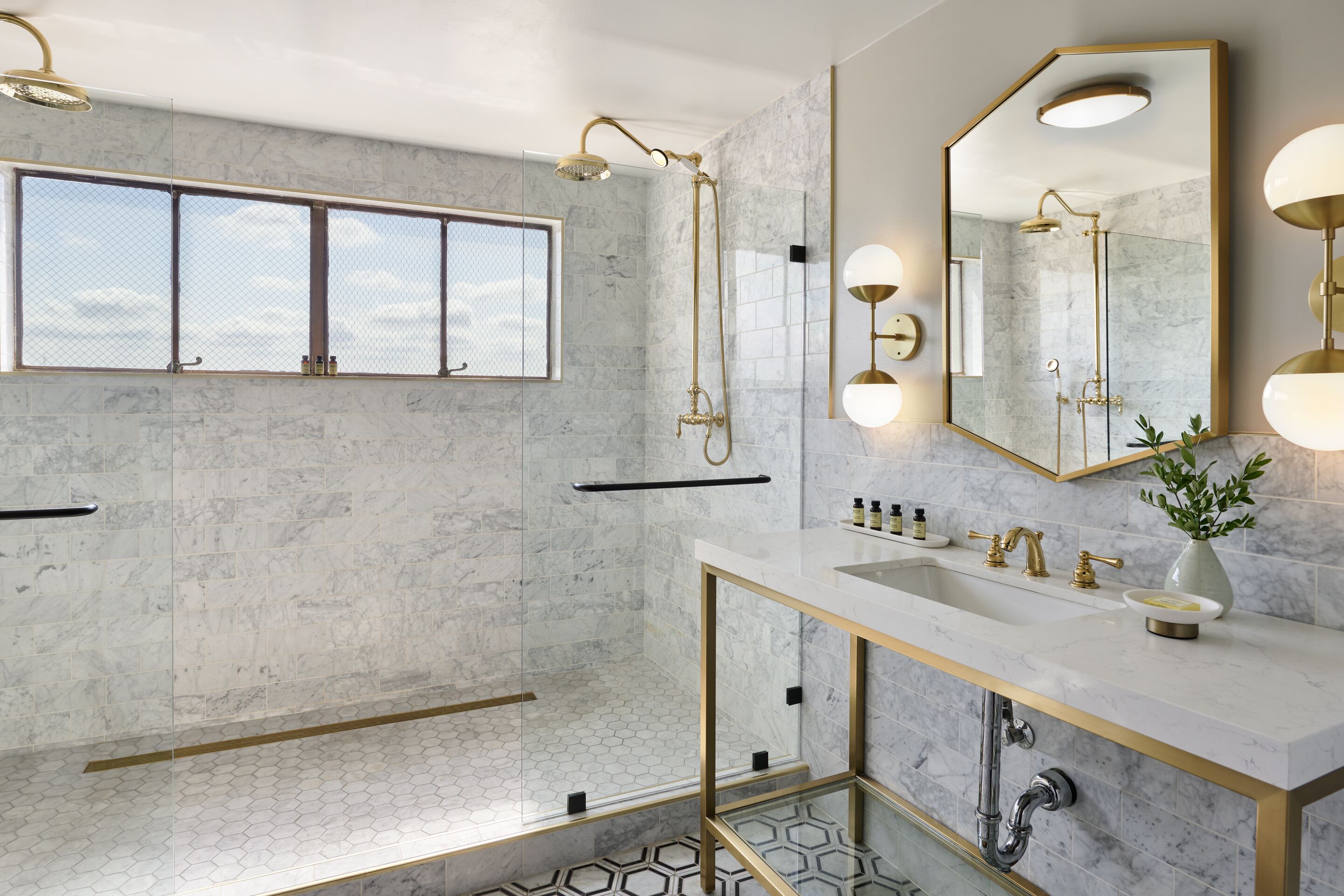 Ein modernes Badezimmer mit einem großen Spiegel, goldenen Armaturen und einem Fenster.