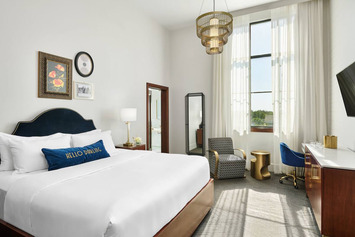 A hotel room with a large bed, a desk, a chair, and a mirror.